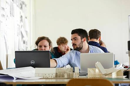 Foto: Studierende der Fakultät Architektur sitzen vor ihren Laptops und einem Modell und arbeiten an einer Projektarbeit
