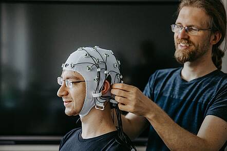 One student wears a cap and the other does an experiment on his brain