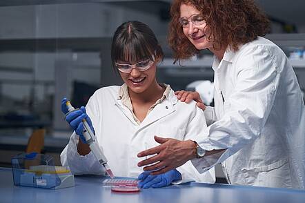 Foto: Eine Studentin arbeitet unter Anleitung mit Pipette und Petrischale