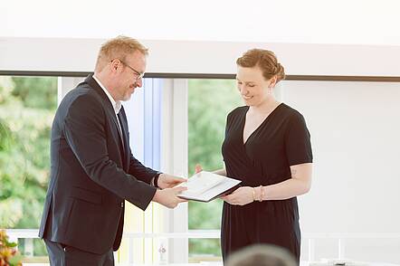 Foto: Lehrender überreicht Studierender das Abschlusszeugnis.