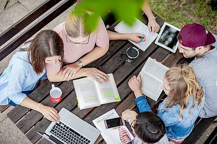 Foto: Studierende sitzen zusammen auf dem Campus und unterhalten sich.