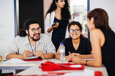 Foto: Gruppe von drei Studierenden an einem Tisch diskutieren