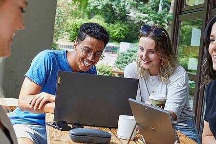 Foto: Studierende der RPTU Kaiserslautern sitzen vor ihren Laptops und lachen und unterhalten sich.