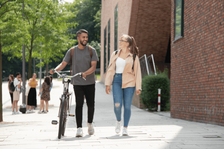 Foto: Studierender unterhält sich mit Studierender und schiebt dabei sein Fahrrad.