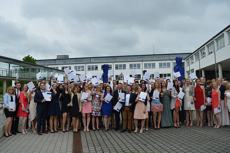 Foto: Eine Gruppe von Absolvent:innen präsentiert jubelnd ihre Abschlusszeugnisse.