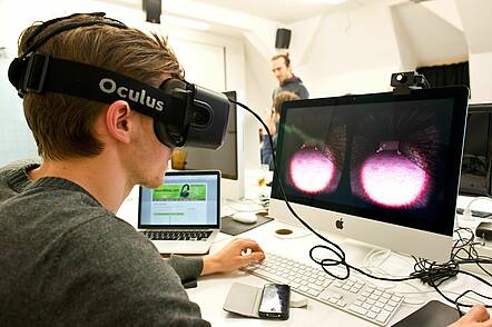 Foto: Studierender trägt eine VR-Brille und arbeitet am Computer