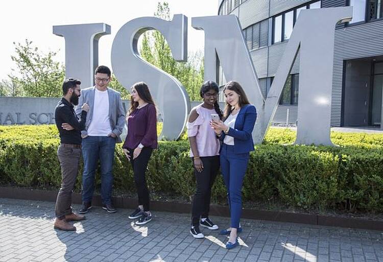 Studierende stehen vor dem Hochschulgebäude der International School of Management und unterhalten sich.